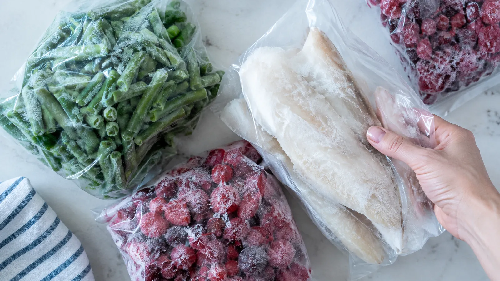 Sachets givrés de haricots verts, fruits rouges et filets de poisson posés sur un plan de travail clair